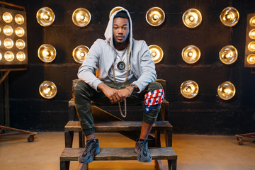Black rapper in hoodie sitting on the steps - obrazy, fototapety, plakaty