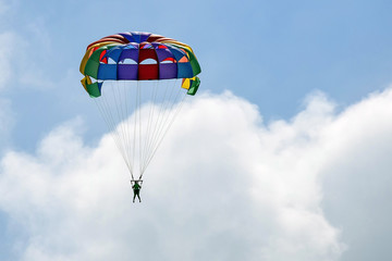 Vacation, extreme sports - colorful parachute over the sky with clouds. One women are flying in the blue sky using multicolored parachute over the sea. Rest on the water. Selective focus. Copy space.