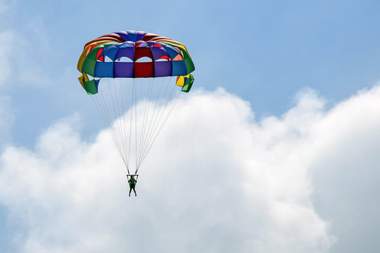Vacation, extreme sports - colorful parachute over the sky with clouds. One women are flying in the blue sky using multicolored parachute over the sea. Rest on the water. Selective focus. Copy space.