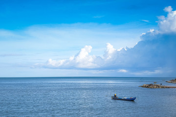 A wooden fishing boat on deep blue sea with some island and cloudy half blue-white sky 