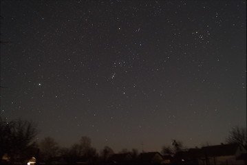 A lond exposure low light photo of village and  night sky. Village far away from city, on sky a lot of stars and constellations. Stock photo of deep sky.