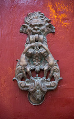 An old style decorative bronze door handle on a wooden red door, the distinctive feature and symbol...