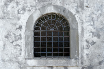 Fototapeta na wymiar Altes halbrundes offenes Gitterfenster in der grauen Fassade eines mittelalterlichen Gebäudes