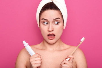 Image of surprised lady with opened mouth, holding toothpaste and toothbrush in hands, posing in...