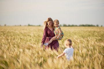Naklejka na ściany i meble Family values. Happy mother and her children spending time together in sunny field. Mom hugging and loving her little kids. Care concept