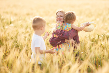 Fototapeta premium Family values. Happy mother and her children spending time together in sunny field. Mom hugging and loving her little kids. Care concept