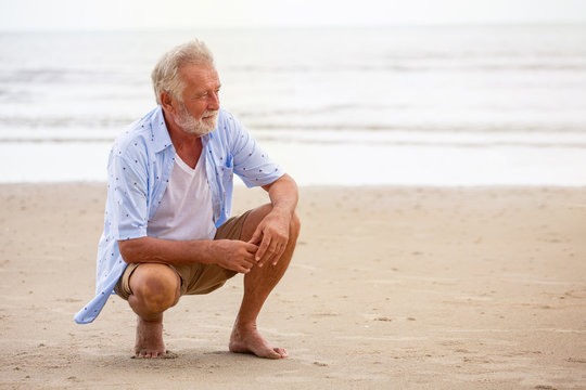 Senior man sitting on beach relaxing . Happy retired man relaxed on sand outdoors