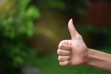 Close-up of human hand with thumb up in front of green background