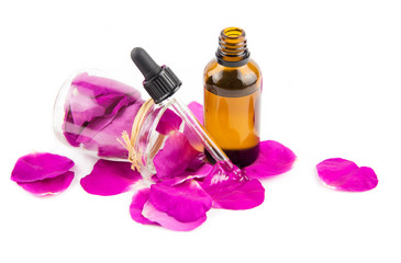 Rose hip petal oil concept. Brown dropper bottle with scattered dark pink rosehip petals and in clear glass jar, isolated white, studio shot.