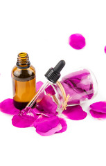 Obraz na płótnie Canvas Rose hip petal oil concept. Brown dropper bottle with scattered dark pink rosehip petals and in clear glass jar, isolated white, studio shot.