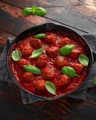 Homemade Meatballs in iron cast with sweet and hot tomato sauce, basil. On wooden table