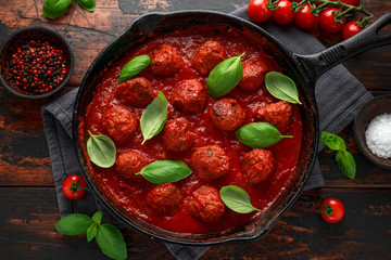 Homemade Meatballs in iron cast with sweet and hot tomato sauce, basil. On wooden table