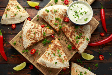 Mexican quesadilla with chicken, corn, black beans, cheese, vegetables, lime and yogurt sauce on wooden board