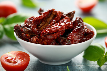 Sun dried tomatoes in white bowl with tomatoes and basil