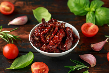 Sun dried tomatoes in white bowl with fresh herbs and spices on wooden table