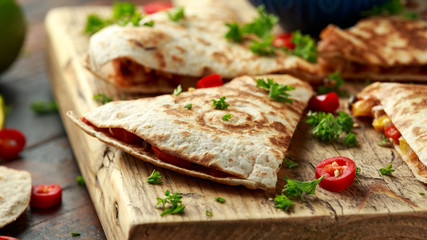 Mexican quesadilla with chicken, corn, black beans, cheese, vegetables, lime and yogurt sauce on wooden board