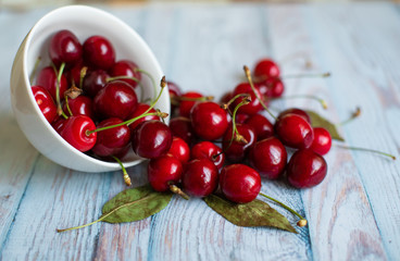 Fresh red cherries in a white plate on a light blue background, space for text, concept of natural fresh vegetarian food