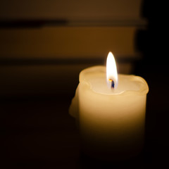 Burning candle on the background of books. Books on the back blurred background. Snapshot in the dark. Flame candles