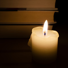 Burning candle on the background of books. Books on the back background. Snapshot in the dark. Flame candles
