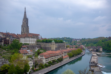Fototapeta premium Beautiful view of aare river with Bern Munster, landmark of Bern, and charming building from Kirchenfeld bridge on cloudy blue sky background