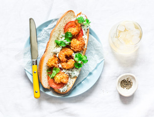 Po' boy sandwich with crispy cornmeal shrimp, tomatoes, cilantro and mayo herbs sauce on light background, top view