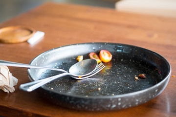 Empty of black ceramic dish with fork and spoon on wooden table
