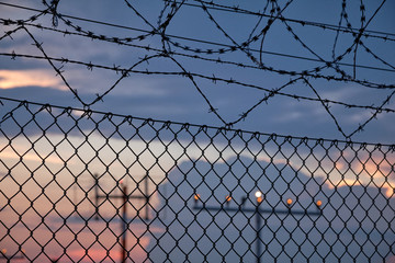Details of a chain link fence with razor wire and in front of a sunset at an airport