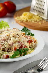 Caesar salad in a white plate on the table with Cutlery, on a background of red tomatoes and grated cheese on a board with a grater