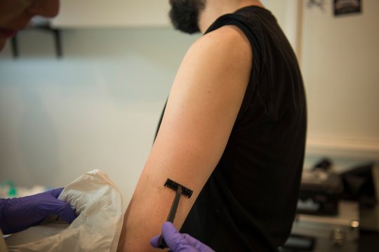 Tattooist shaves the arm of a young man who will be tattooed