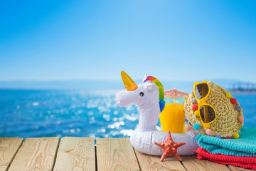 Summer vacation concept with orange juice, beach accessories and unicorn pool float over sea beach background © maglara