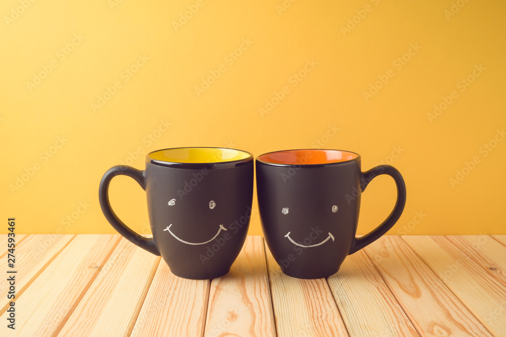 Wall mural chalkboard coffee mugs on wooden table with funny cute faces. friendship day concept