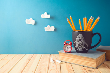 Back to school background with pencils, rocket chalkboard sketch, books and alarm clock on wooden table
