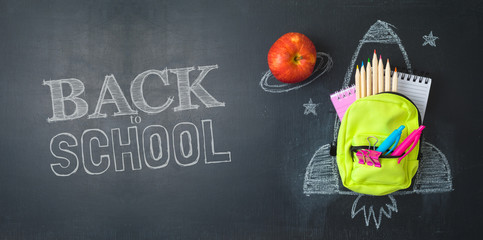 Back to school concept with small bag backpack, school supplies and rocket sketch over chalkboad...