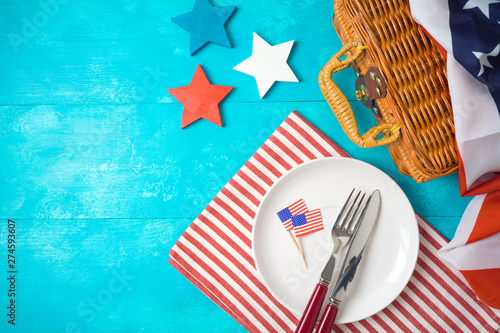 Happy Independence Day, 4th of July celebration concept with picnic basket, plate and USA flag on wooden background.