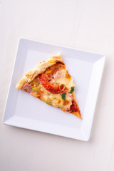 Single pizza slice on white plate wooden background top view