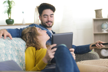 couple relaxing on sofa using tablet and watching tv