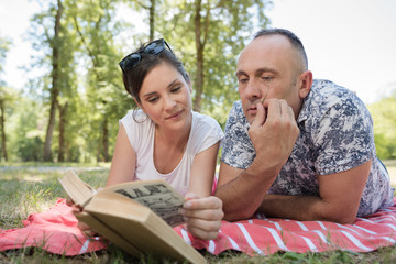 middle aged couple layed on blanket looking at book