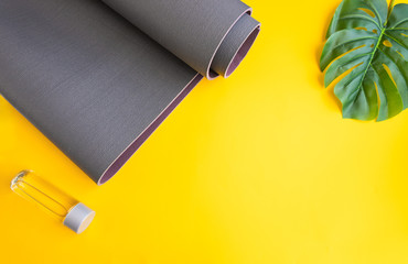 Close up of grey exercise mat and water bottle on yellow background with palm leaf. Concept for...