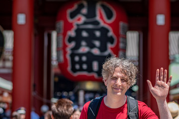 An adventurous tourist waves while visiting Senso Ji Temple in Tokyo, Japan. The symbol on the lantern is the name of the town, Kobunacho, which donated it.