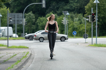 Junge Frau mit Elektroroller im Stadtverkehr an Kreuzung mit Ampel 1/2