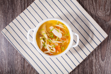 Chicken soup on a wooden background with a linen towel in a white tureen