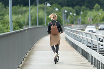 Junge Frau fährt mit Elektroroller auf Radweg über Brücke 2/2