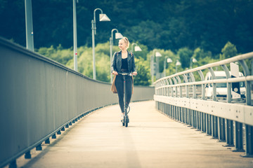 Junge Frau fährt mit Elektroroller auf Radweg über Brücke 1/2