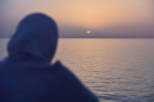 Arab Woman In Traditional Muslim Hijab Or Jilbab Looking On The Beautiful Golden Sunset In The Sea From The Big Ship. Back View. Peaceful Serene Landscape. Middle East.