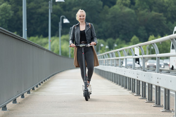 Junge Frau fährt mit Elektroroller auf Radweg über Brücke 2/2