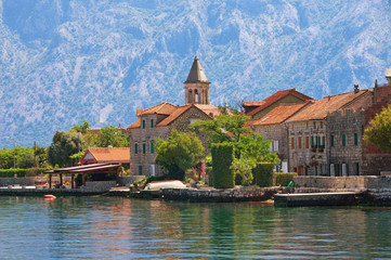 Fototapeta premium Small seaside village in the background of the mountains. Montenegro, Adriatic Sea. View of Bay of Kotor and Stoliv village on sunny summer day