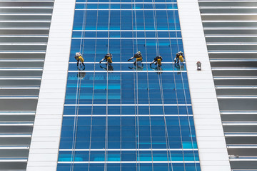 Group of workers wearing safety harness clean windows at height on modern high rise building. Professional rope access. Low angle view
