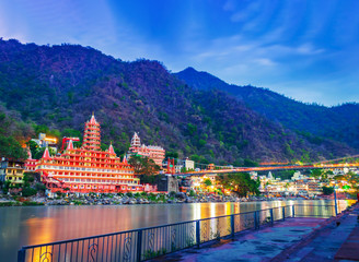   River Ganges, the famous bridge Laxman Jhula  surrounded by temples and mountains around in rishikesh, India 