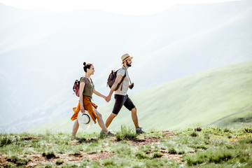 Beautiful couple walking with backpacks on the green meadow, while traveling in the mountains...