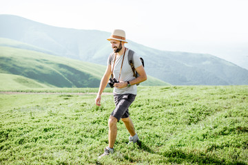 Man hiking with backpack on the beautiful green meadow while traveling in the mountains during the sunny weather
